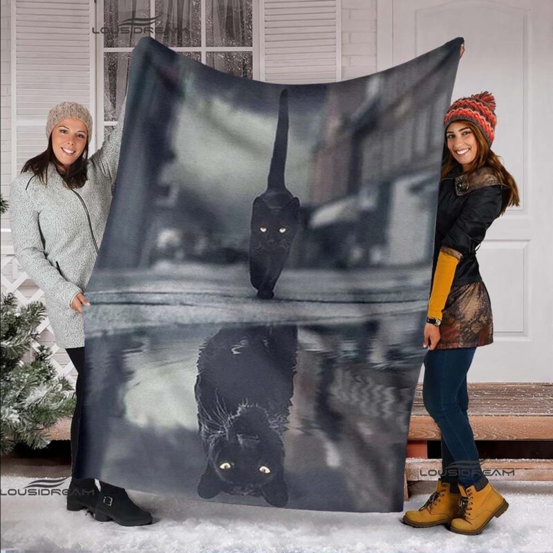 deux jeunes femmes tiennent ouvert pour que l'on voit le motif, un plaid avec un chat noir en train de marcher et dont son reflet est une panthère noire