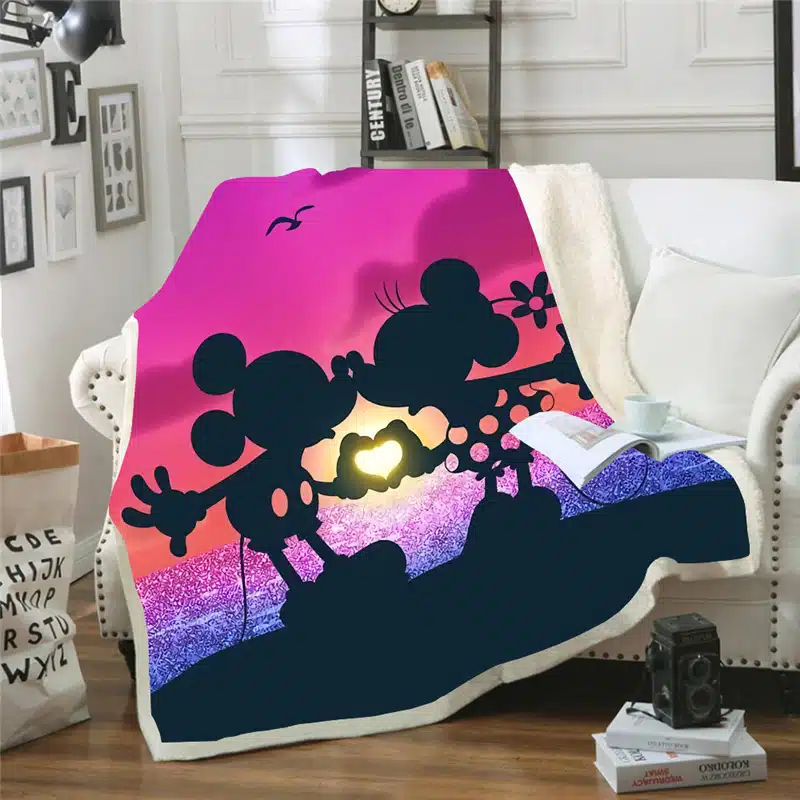 sur un canapé blanc dans un salon , un plaid est installé et représente Mickey et minnie en train de s'embrasser devant un coucher de soleil