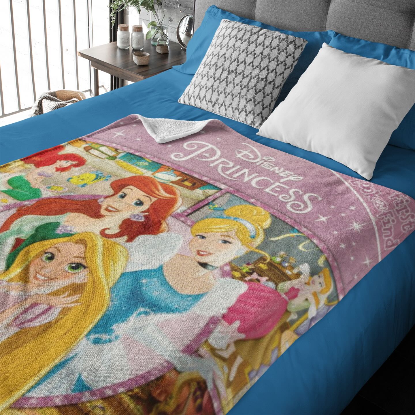 Un plaid de princesse disney posé sur un lit à la couverture bleue et la tête de lit grise.