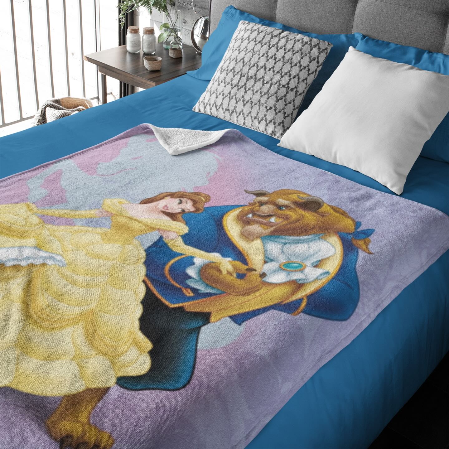 Un plaid la belle et la bête posé sur un lit à la couverture bleue et la t^te de lit grise.