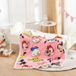 Plaid Disney de couleur rose avec des têtes en cartoons de personnages, posé sur un lit pour enfant blanc avec un sol en parquet