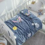 Plaid Disney de Dumbo de couleur bleu, posé sur un lit d'enfant avec des draps blancs
