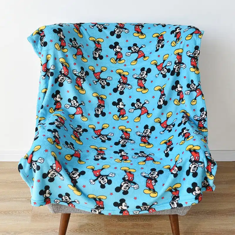Plaid Disney de couleur bleu avec des motifs de Mickey, posé sur une chaise devant un mur blanc et sur parquet