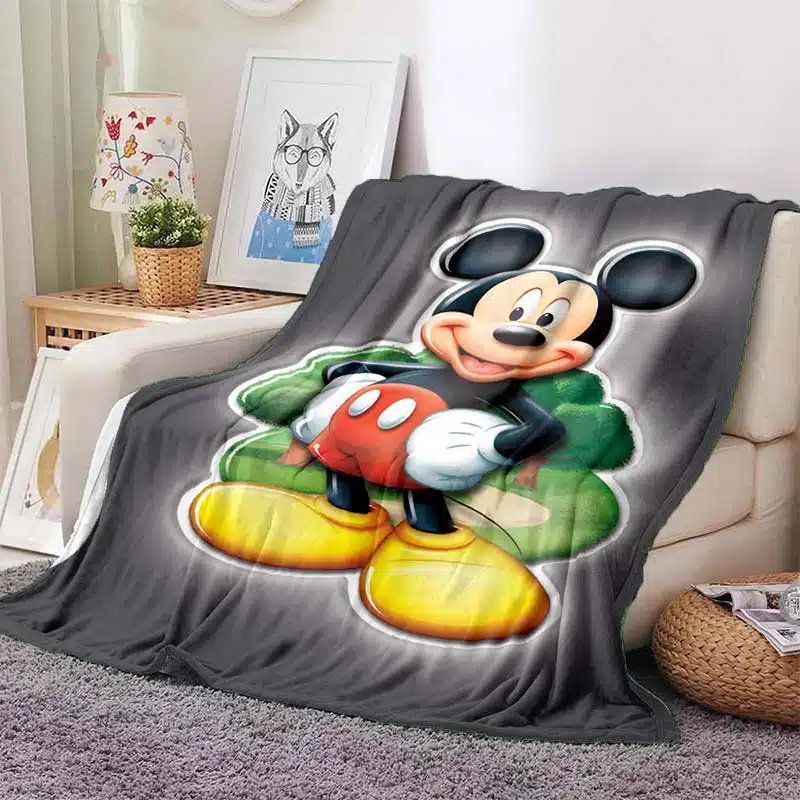 Plaid Mickey représentant Mickey avec un paysage vert sur fond noir, posé sur un canapé de couleur beige