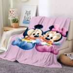 Plaid Mickey en forme de bébé avec Minnie sur fond rose, posé sur un canapé beige