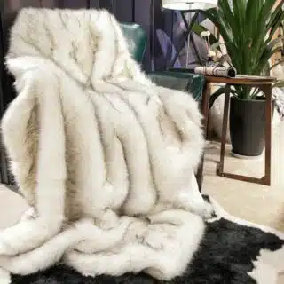 Plaid fausse fourrure renard polaire posé sur un fauteuil en cuir, dans un salon.