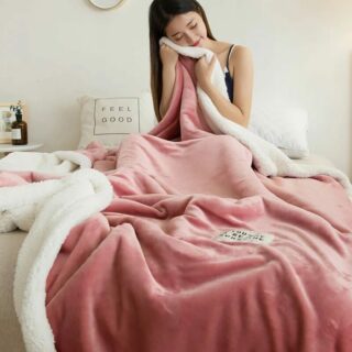 Couverture douceur sherpa en version rose foncé, sur un lit dans une chambre à coucher. La jeune femme se caresse la joue pour tester sa douceur.