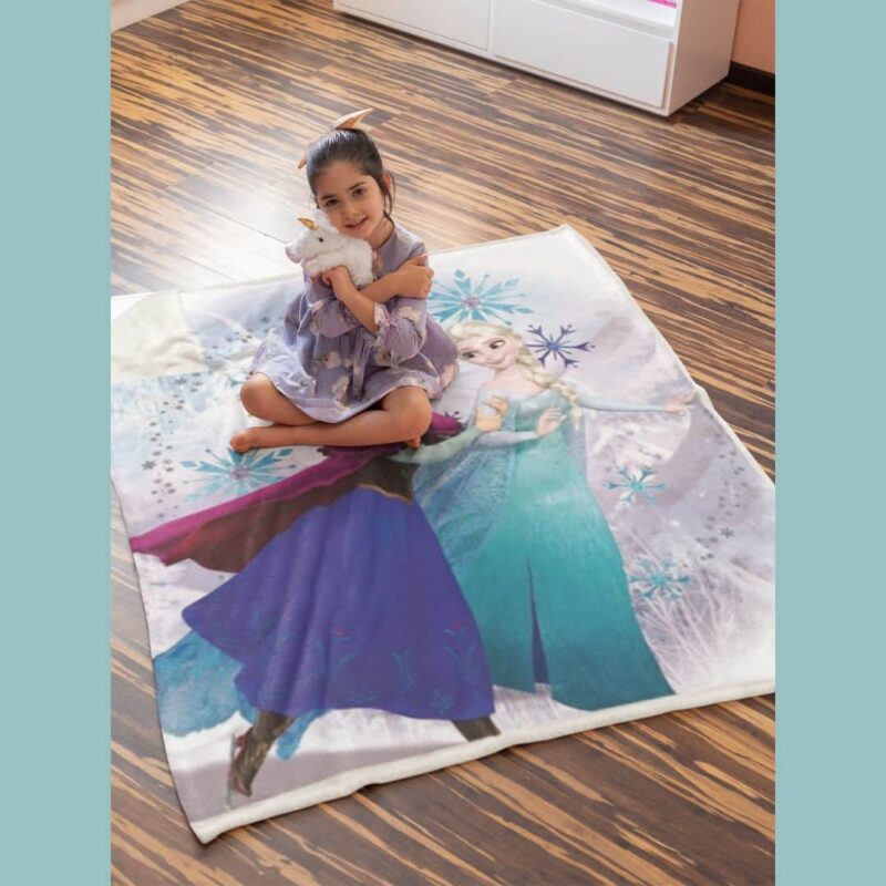 Petite fille installée sur la couverture moelleuse et pelucheuse Anna et Elsa, par terre au milieu de sa chambre.