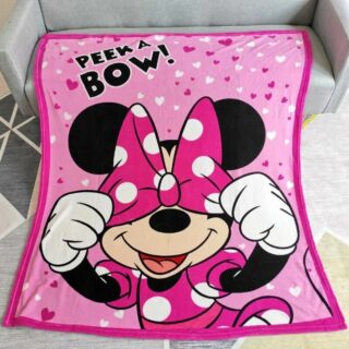 Plaid Minnie rose vif dont l'imprimé represente Minnie qui se cache les yeux derrière son nœud, étalé sur un canapé gris dans un salon.