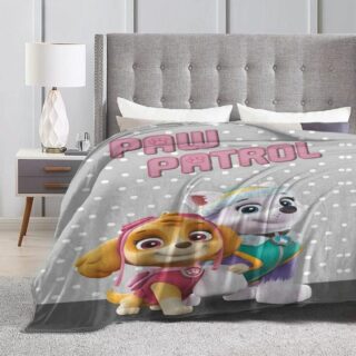 Plaid gris Pat Patrouille qui se compose de Stella et Everest qui se tiennent par la patte, placé sur un lit dans une chambre.