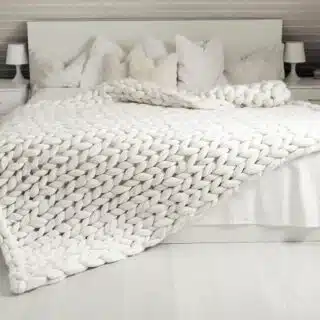 Plaid grosse maille blanc déposé sur un lit dans une chambre à coucher.