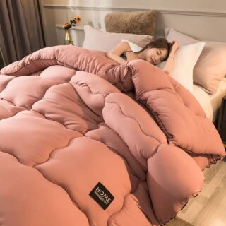 Une jeune femme est dans son lit, confortablement installée avec l'édredon doux cocon de pêche rose foncé, dans sa chambre à coucher.